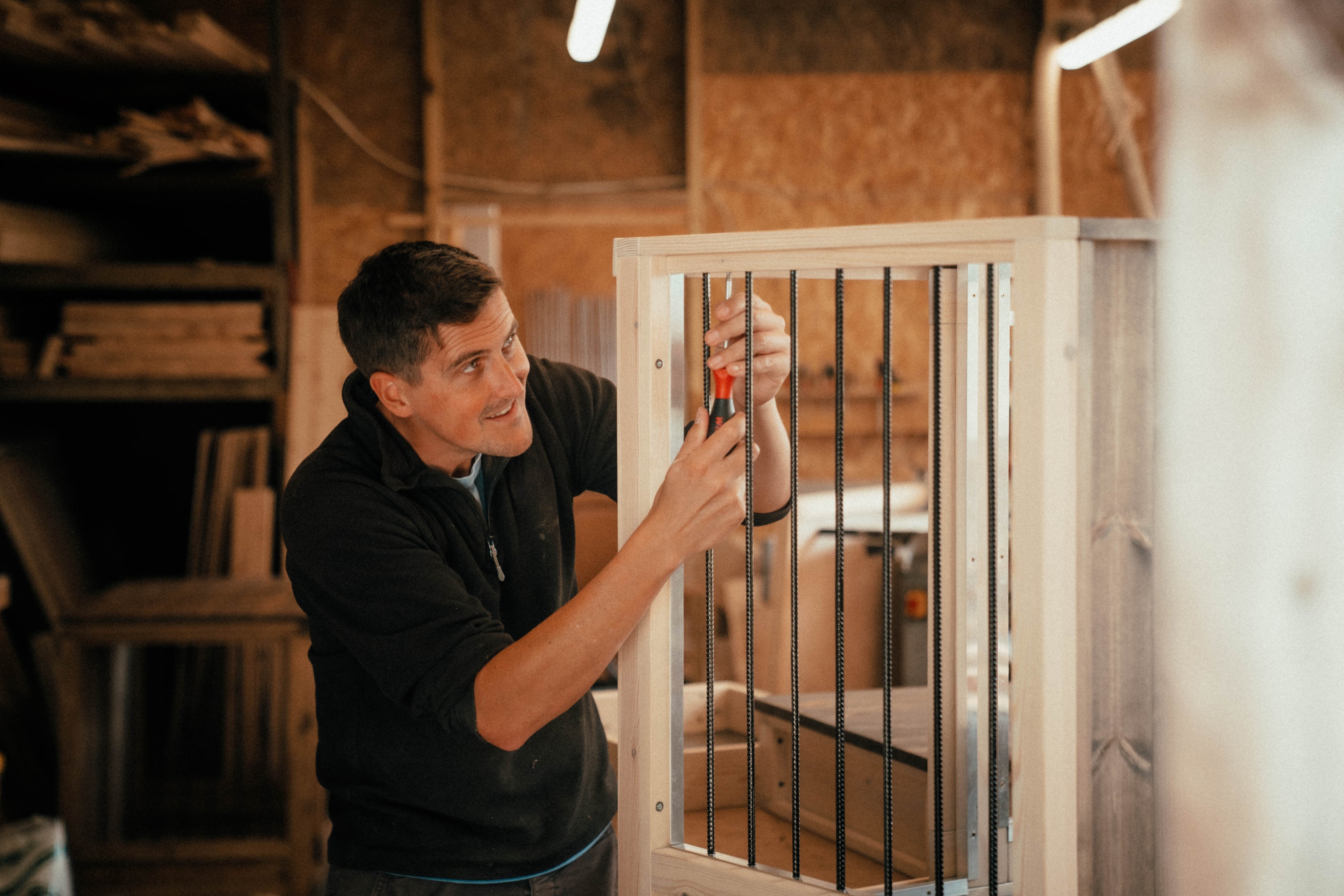 Master carpenter at Countryside Carpentry, handcrafting a custom wooden dog crate with metal bars in the workshop, showcasing high-quality, handmade dog furniture.