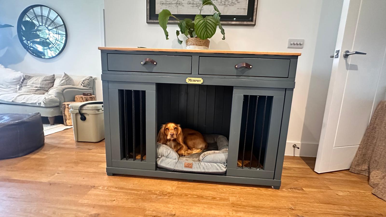 Dog inside a gray wooden pet crate with a wooden top in a living room.