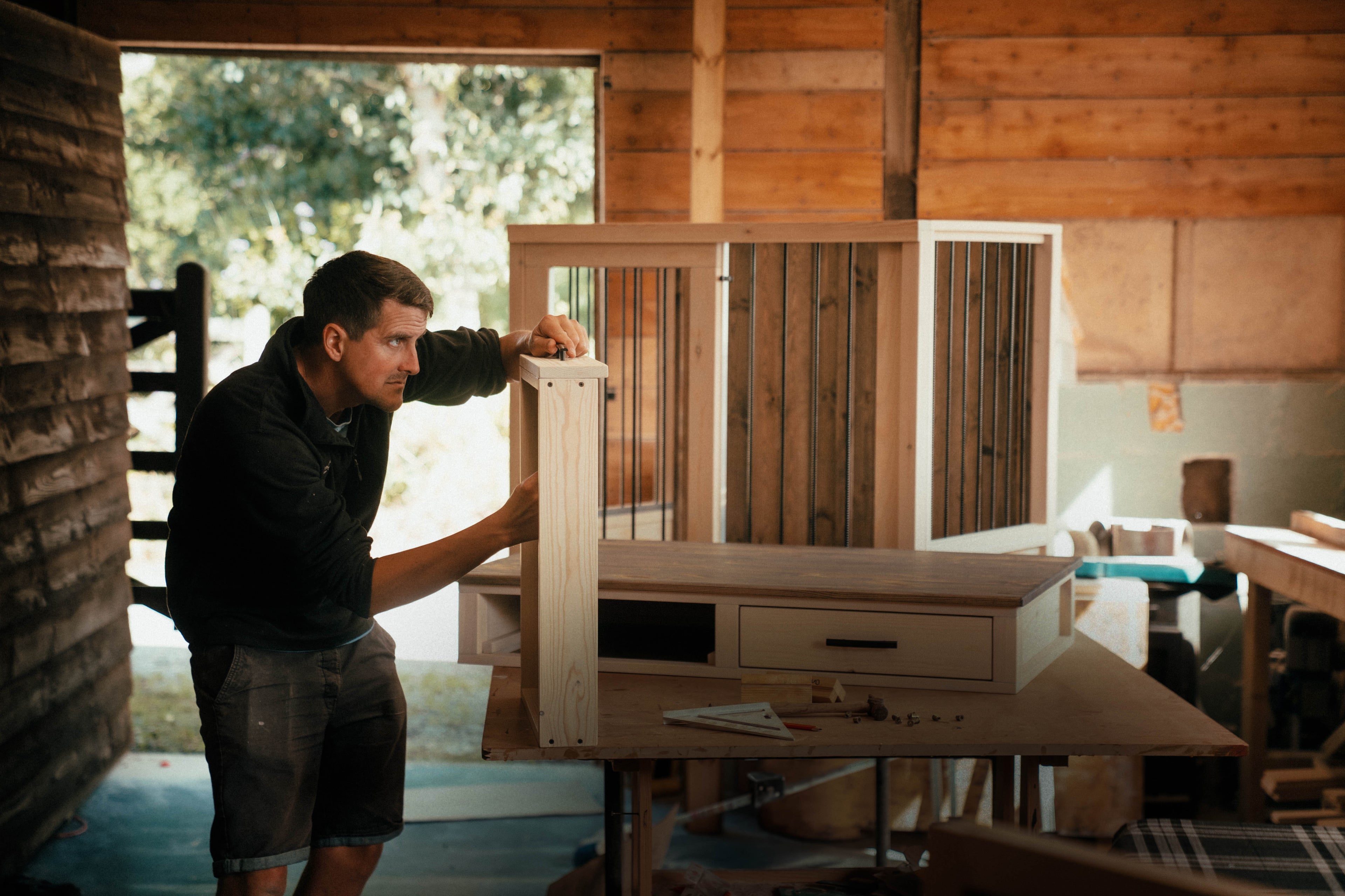 Man assembling a custom wooden dog crate in a rural workshop, showing the handmade craftsmanship behind premium indoor dog crate furniture.